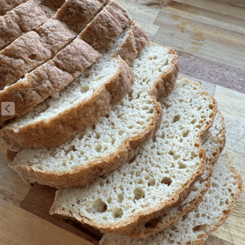 10 slices of gluten free fresh milled sandwich bread (yeast) laying on a wooden countertop (acacia). The crumb of the bread is showing on 5 of the slices with varying sizes of holes and a brown crust.