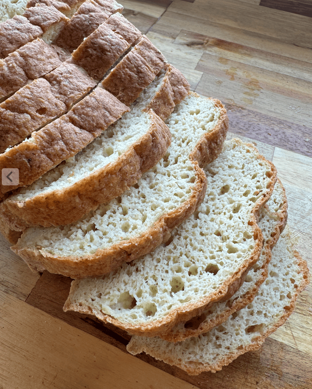 10 slices of gluten free fresh milled sandwich bread (yeast) laying on a wooden countertop (acacia). The crumb of the bread is showing on 5 of the slices with varying sizes of holes and a brown crust.