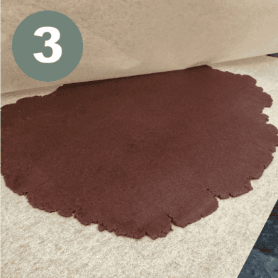 A piece of brown parchment paper lifted with a brown circle underneath on top of another piece of parchment paper with a green circle with a white number 3 in the upper lefthand corner 