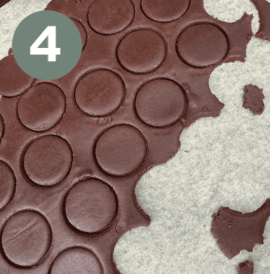 Brown dough with small circle indents on top of a piece of parchment paper with a green circle with a white number 4 in the upper lefthand corner 