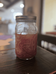 Honey Pickled Onions in a sealed mason jar on a brown table.