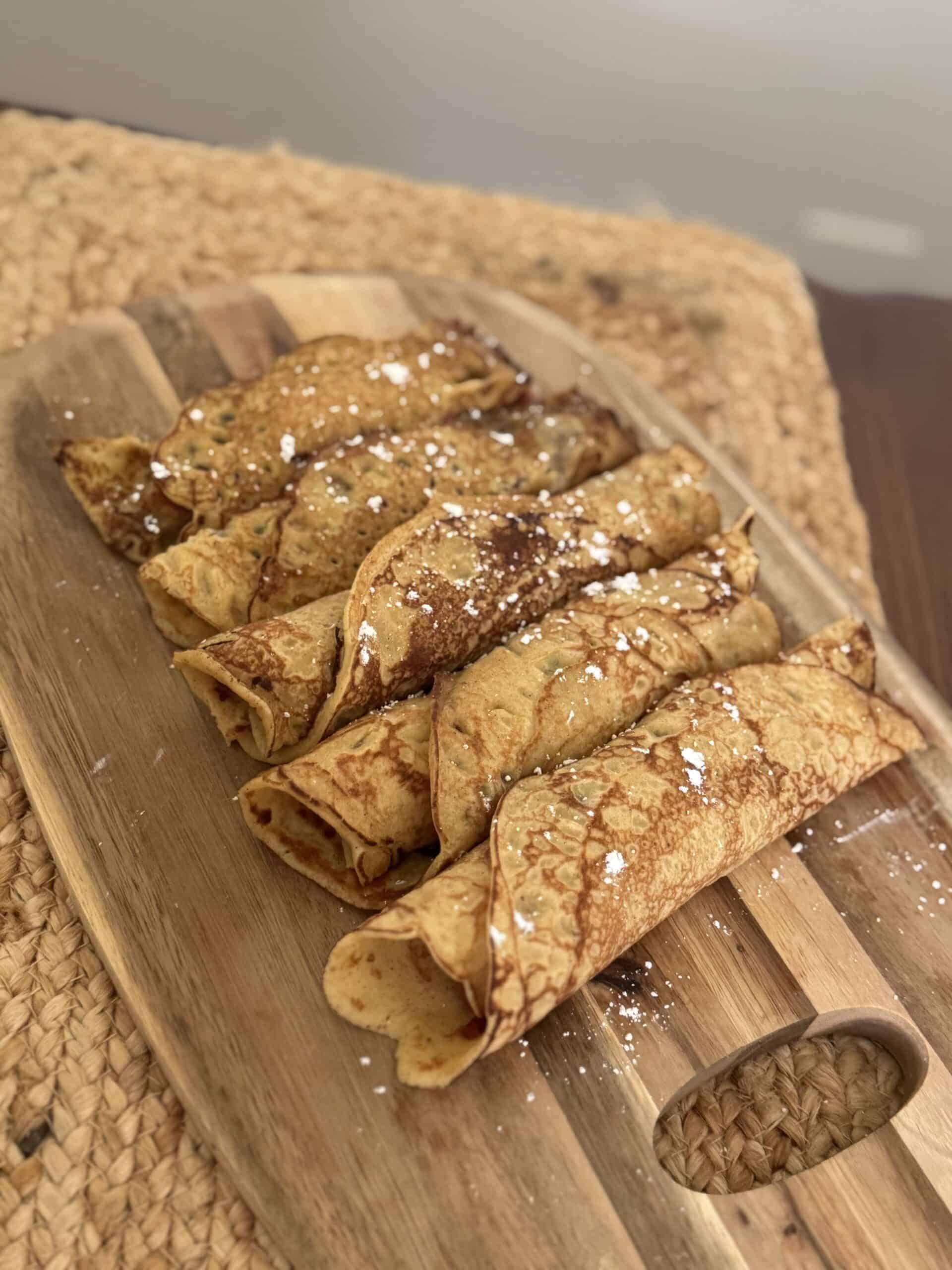 Delicious gluten-free crepes rolled on a wooden cutting board with powdered sugar. 