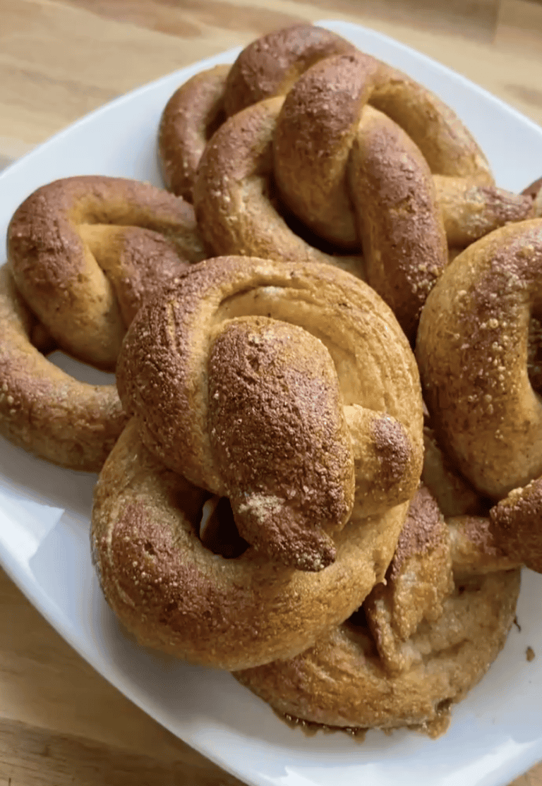 A pile of 6 soft, fluffy gluten free pretzels on a white plate sitting on a wooden countertop.