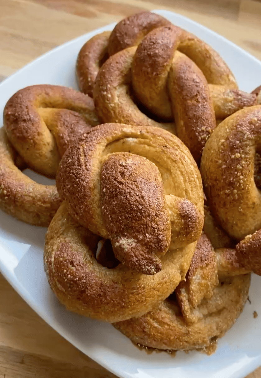 A pile of 6 soft, fluffy gluten free pretzels on a white plate sitting on a wooden countertop.
