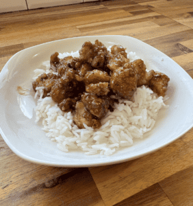 Crispy gluten-free sesame chicken served over white rice on a white plate.