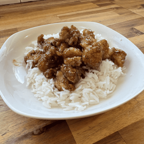 Crispy gluten-free sesame chicken served over white rice on a white plate.