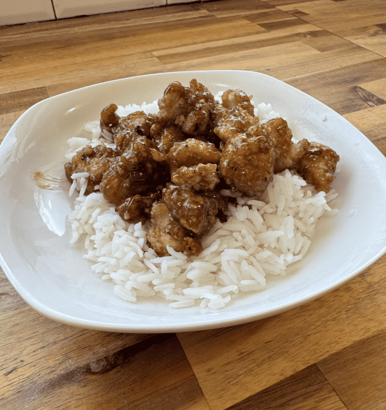 Crispy gluten-free sesame chicken served over white rice on a white plate.