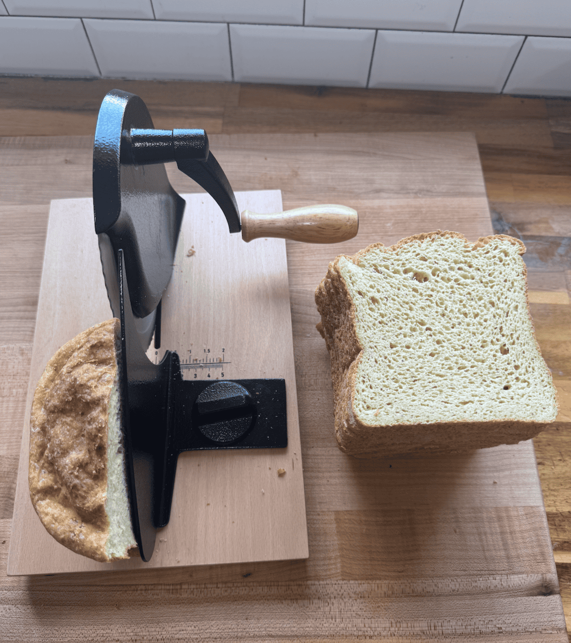 A stack of sliced bread next to a bread slice with a black handle and partial loaf of bread on brown kitchen counter.