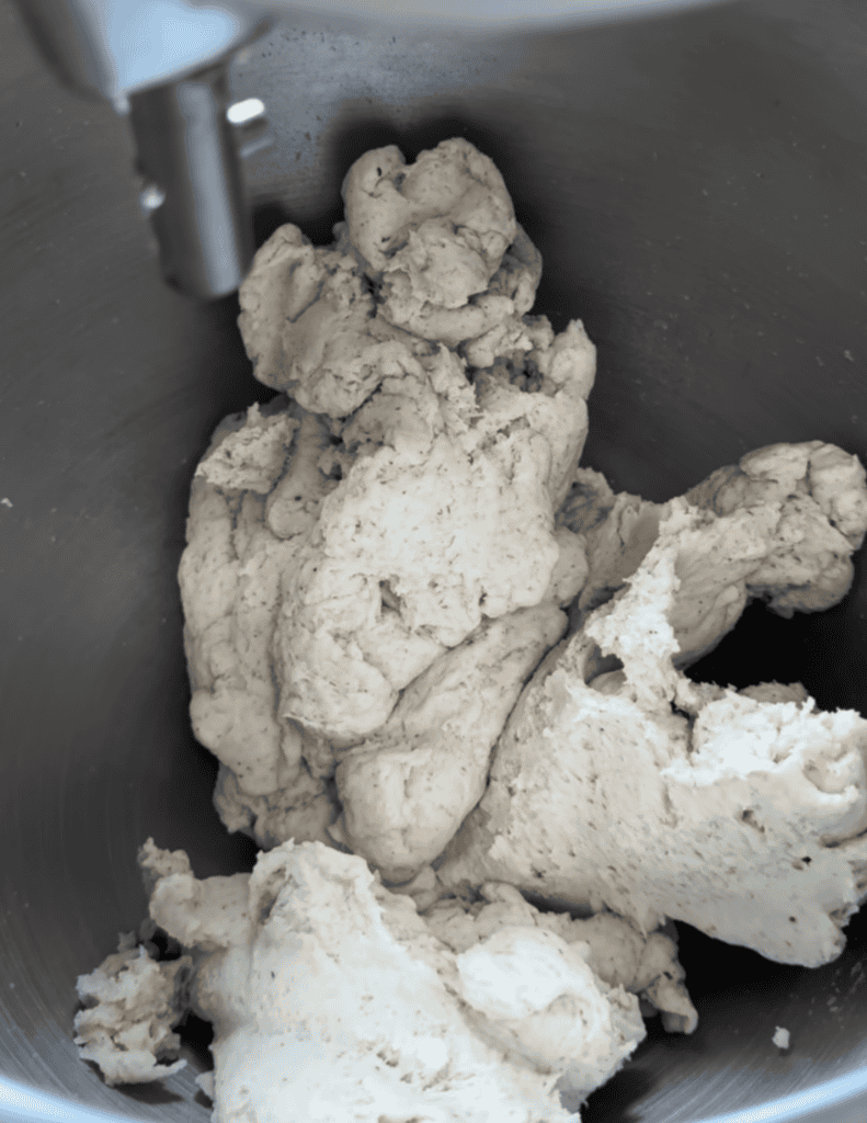 The inside of a metal bowl with a white dough mixture inside and a metal bar in the upper left hand corner