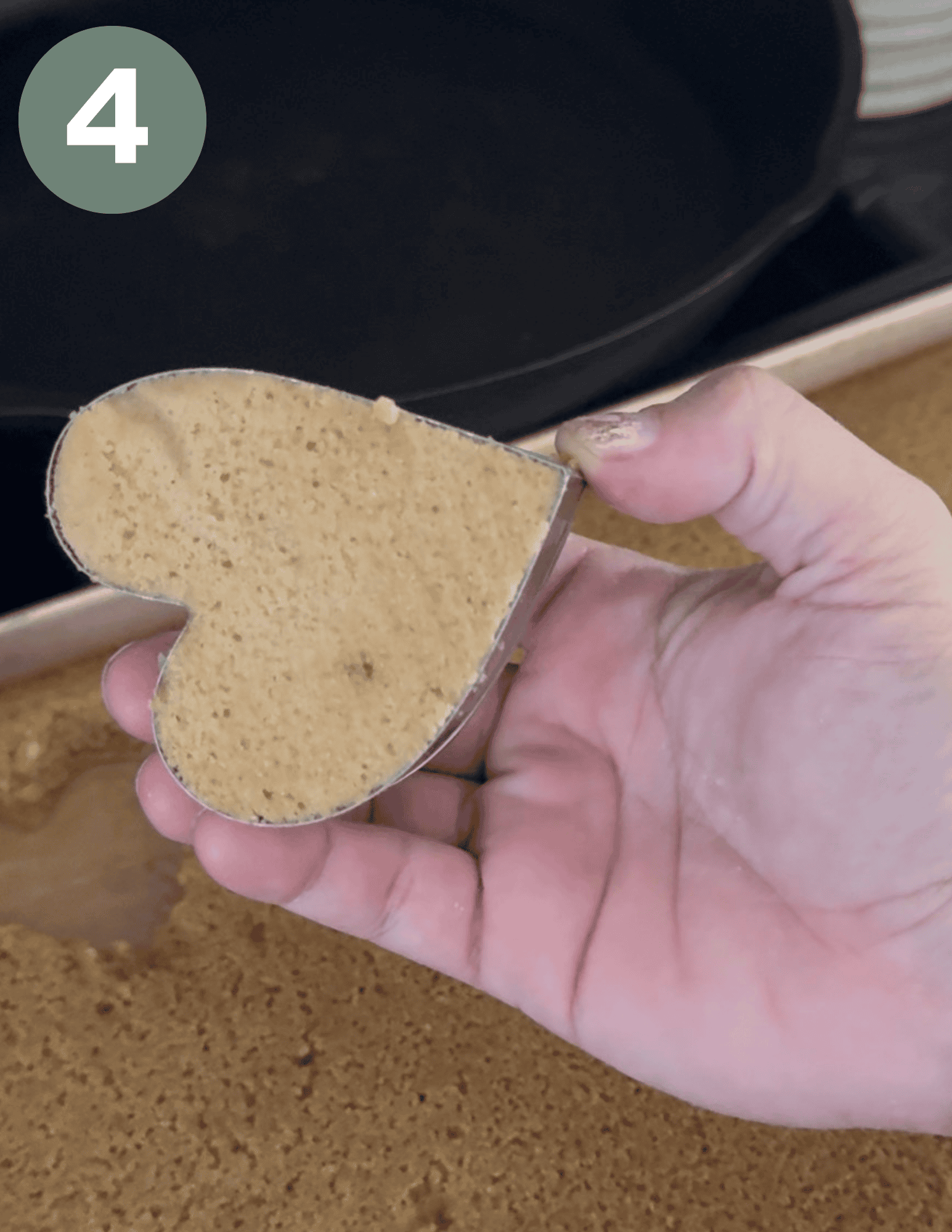 Hand holding a heart-shaped cake mold filled with gluten-free cake batter.