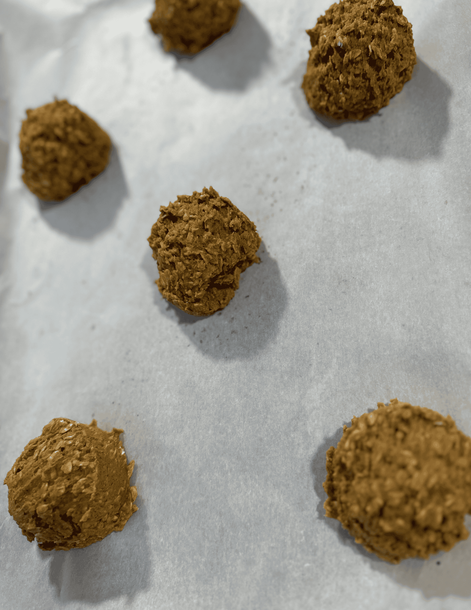 Six balls of dough evenly spread apart on a piece of white parchment paper