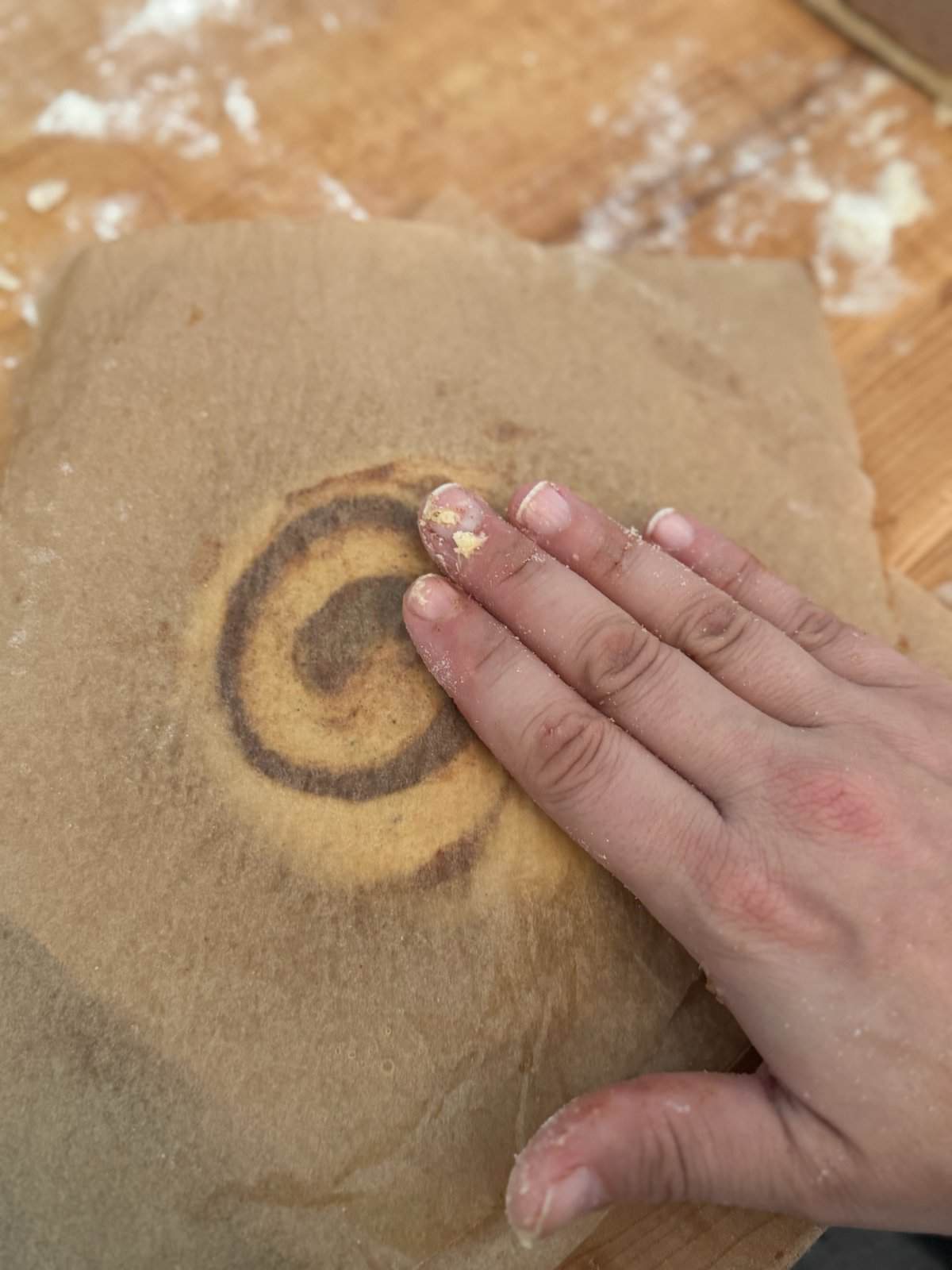 A hand patting a raw circle of gluten free dough with cinnamon filling with parchment paper on top