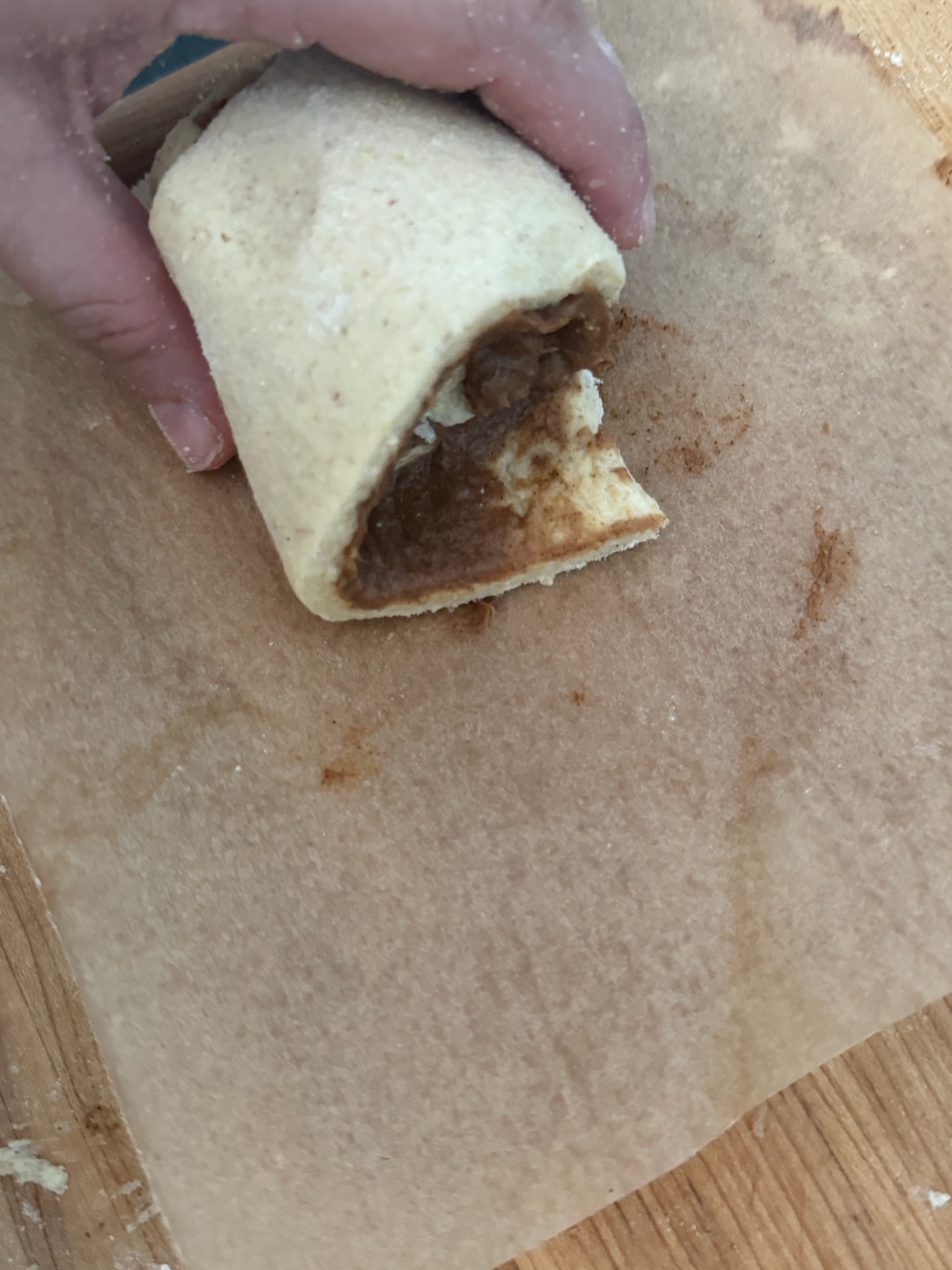 Roll of raw dough with cinnamon paste filling with the edge of the dough sticking out