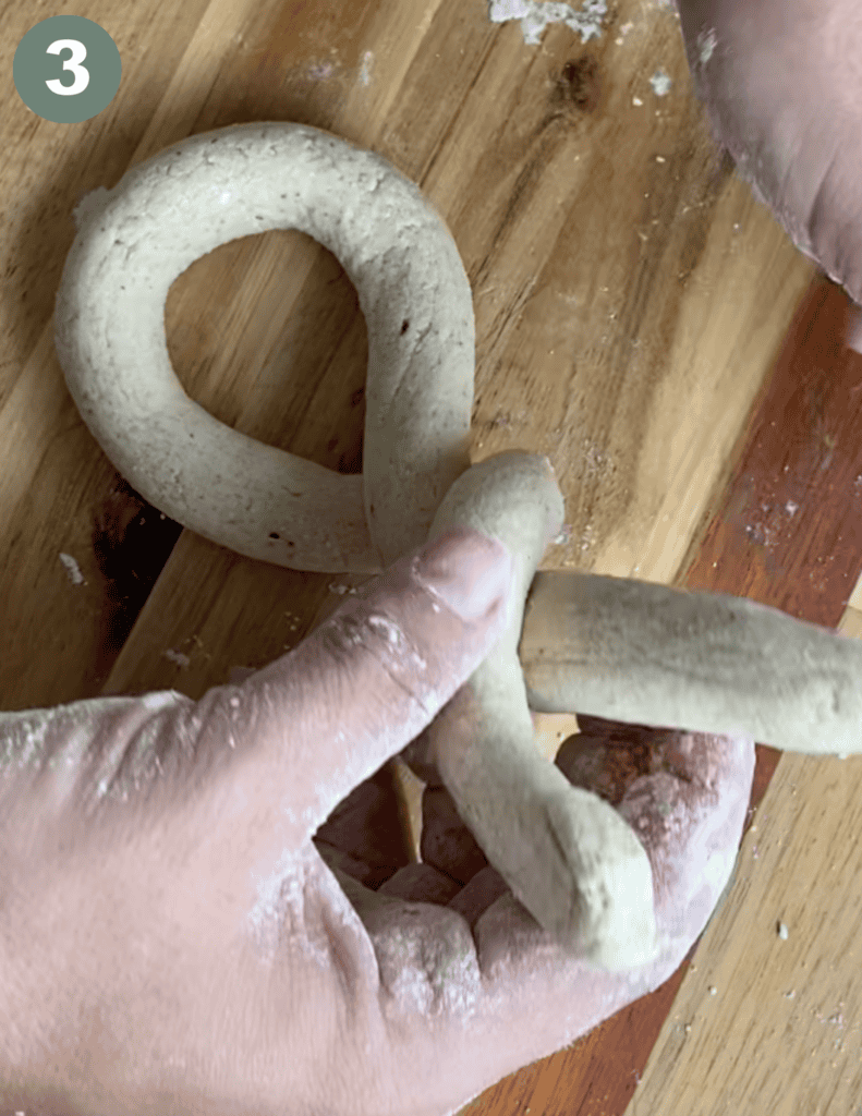 Hand shaping a gluten-free soft pretzel dough on a wooden surface.