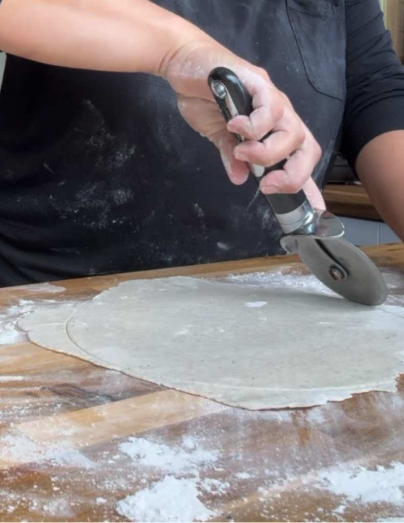 Using a pizza cutter to shape the gluten free torilla into a circle.